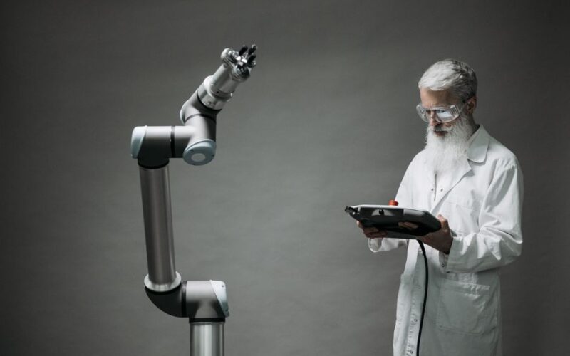 A scientist in a lab coat operates a high-tech robotic arm in a laboratory setting.