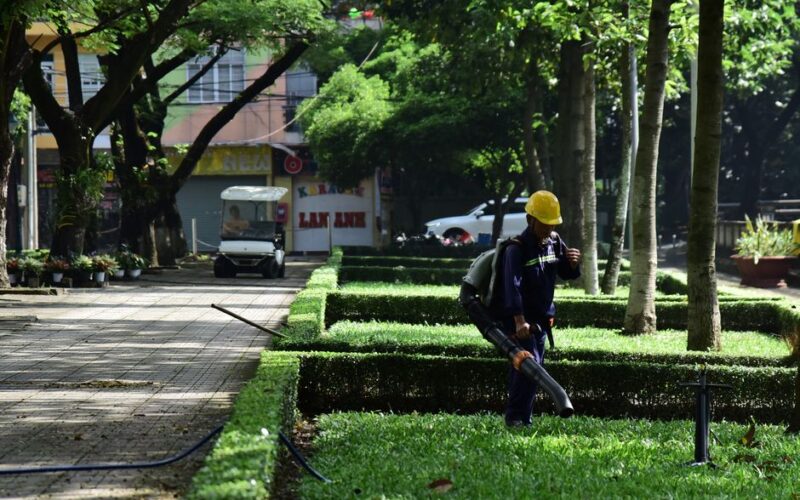 A gardener in uniform uses a leaf blower to maintain a city park's greenery, emphasizing urban cleanliness.