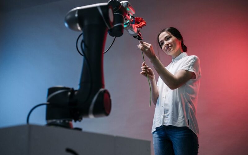 A woman and a robot arm collaboratively holding a flower, symbolizing technology's gentle touch.