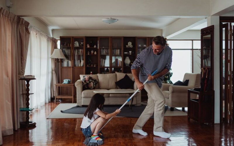 A playful moment as a father and daughter clean their living room, enhancing family bonding through chores.