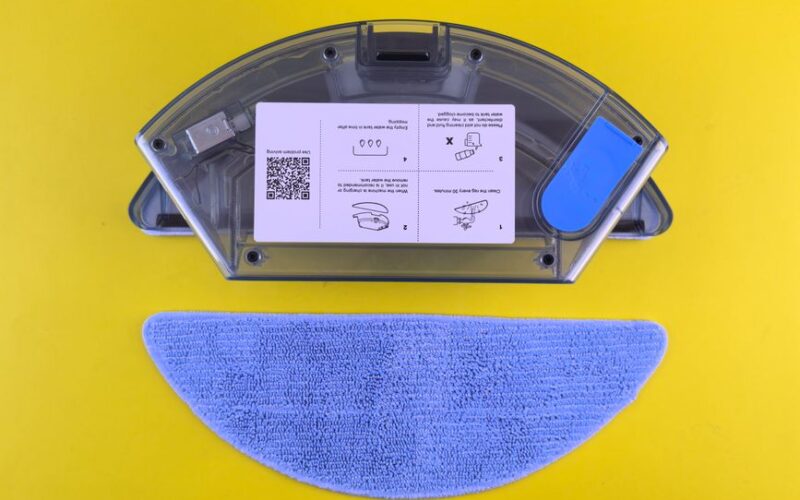 Cleaning robot water tank and mop on yellow backdrop, showcasing household appliance detail.