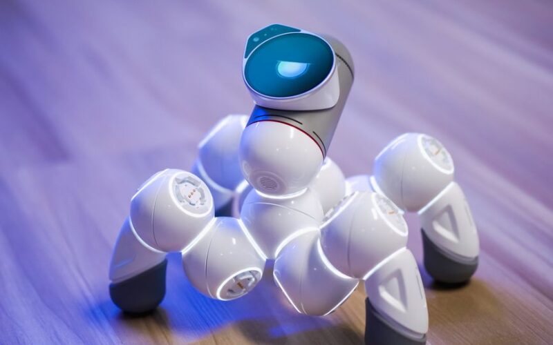 A sleek, white robotic toy on a wooden floor with a blurred background and blue lighting.