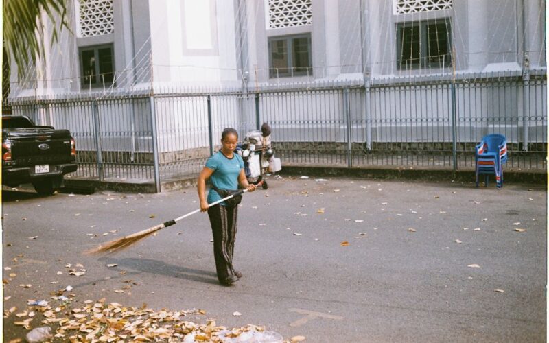 A woman sweeping leaves on a street in Ho Chi Minh City, showcasing daily urban life.