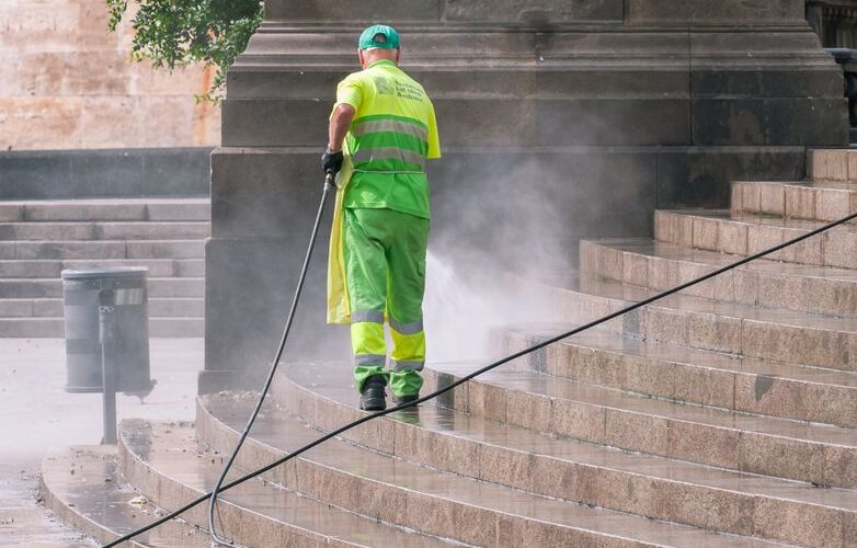 A municipal worker power washing stone steps outdoors, ensuring cleanliness and maintenance.