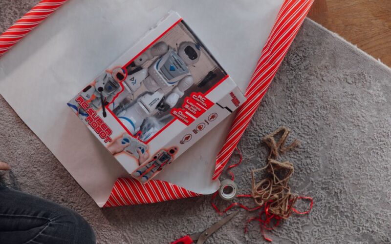 A remote control robot toy being wrapped as a Christmas present on a cozy carpet.