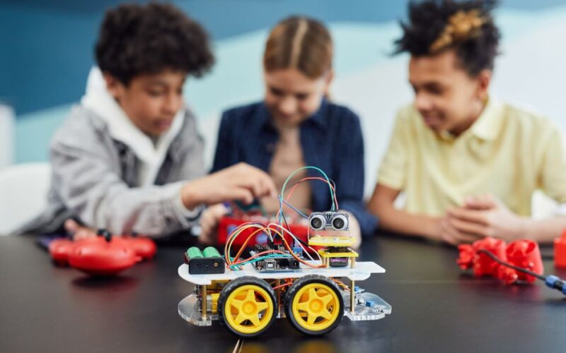Children collaborating on a robotics project, building a small robot car in an educational setting.
