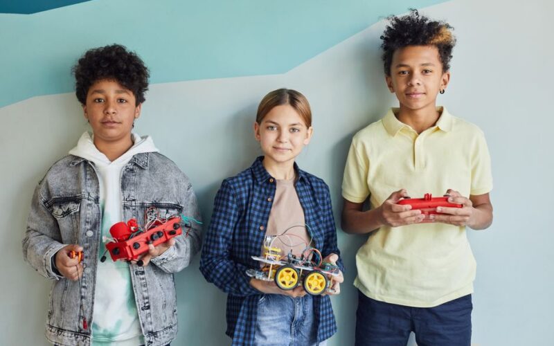 Three children holding robotic projects, showcasing diversity and teamwork.