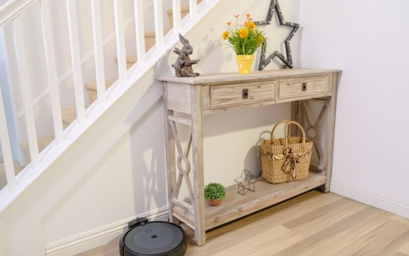 Stylish home hallway with a robotic vacuum and decorative wooden table under stairs.