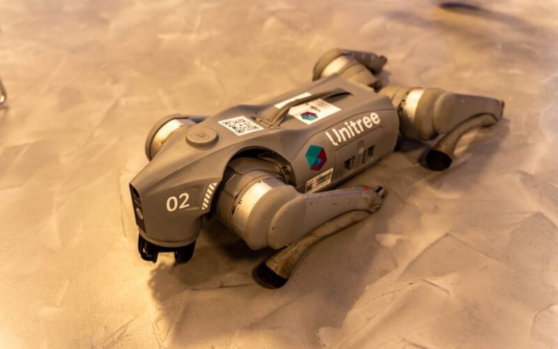 A Unitree robot dog resting on an indoor concrete floor.