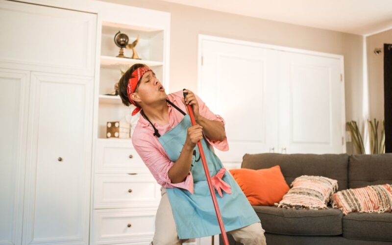 Cheerful man cleaning and singing into a broom at home, creating a fun atmosphere.