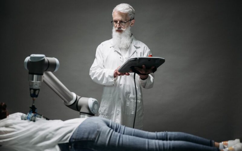 A scientist controls a robotic arm conducting research on a person lying down.