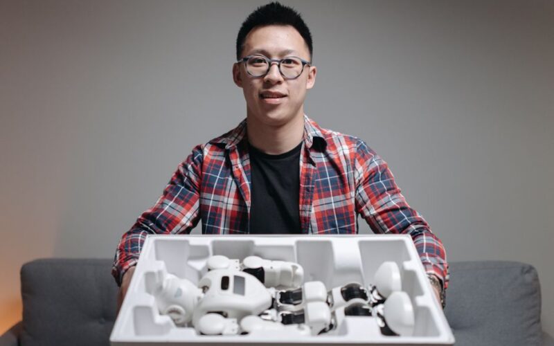 Asian man holding a box with robot components, showcasing technology and innovation indoors.