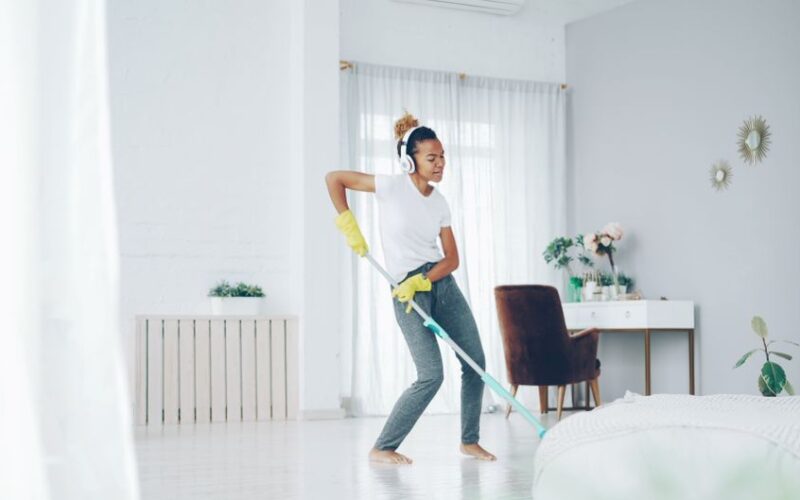 Cheerful young woman dances while mopping her bright, modern living room.