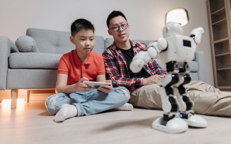 A father and his son bonding while playing with a robot and remote control indoors.