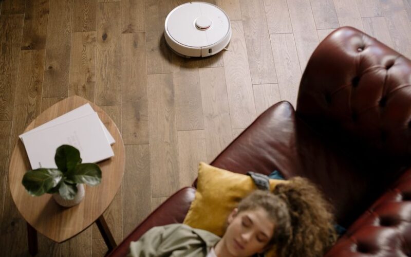 A modern living room with a robotic vacuum and a woman resting, showcasing ease and comfort.