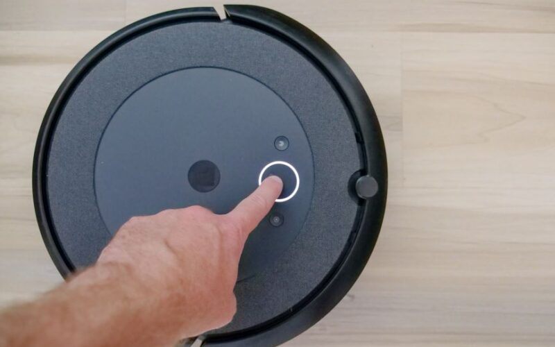Close-up of a finger pressing a start button on a robotic vacuum cleaner at home.