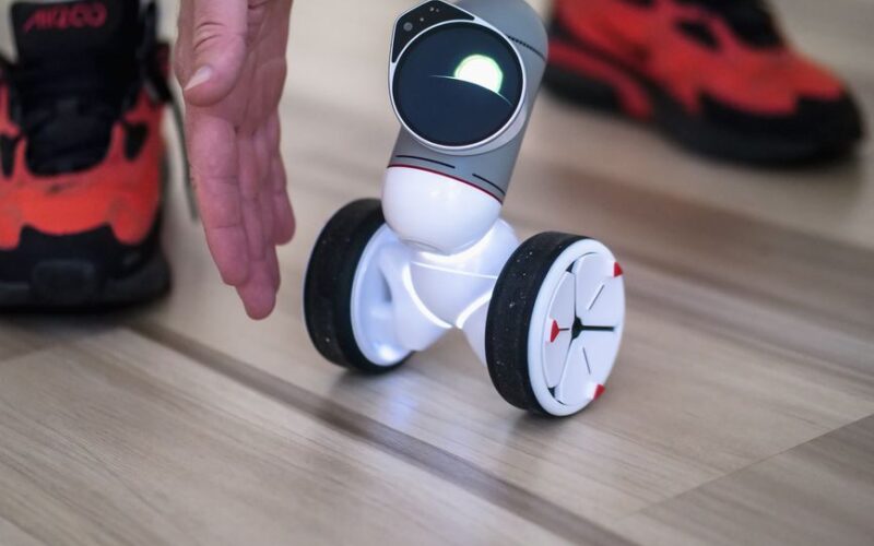 Close-up of a small innovative balancing robot with a human hand and sneaker in view.