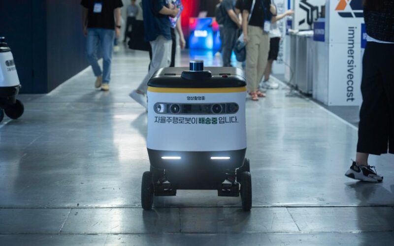 Autonomous delivery robot navigating indoors during a technology event.