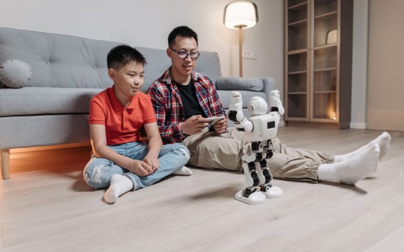 Father and son enjoy bonding time controlling a robot in a cozy living room setting.