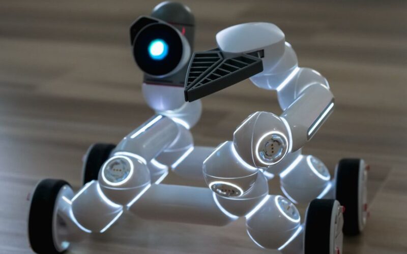 Close-up of a wheeled robot toy with LED lights on a wooden floor indoors.