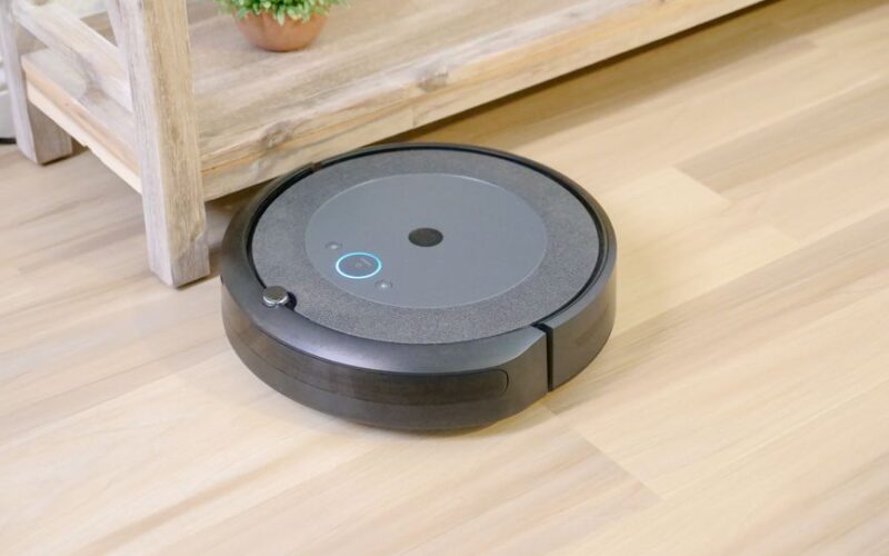 Automated robotic vacuum cleaner on hardwood floor next to plant.