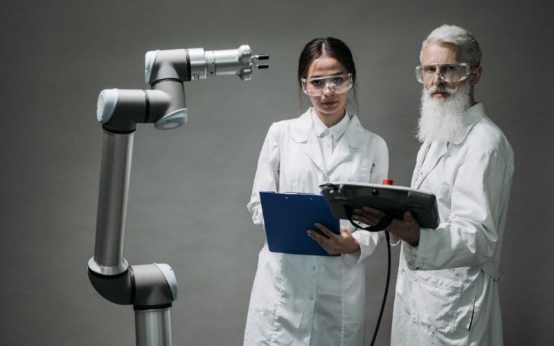 Two scientists in lab coats analyzing a robotic arm in a laboratory setting.