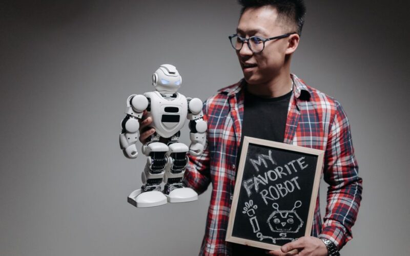 Asian man holding a robot and chalkboard with 'My Favorite Robot' written on it.