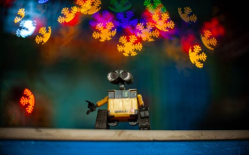 Toy robot capturing colorful bokeh lights in a vibrant, festive indoor setting.