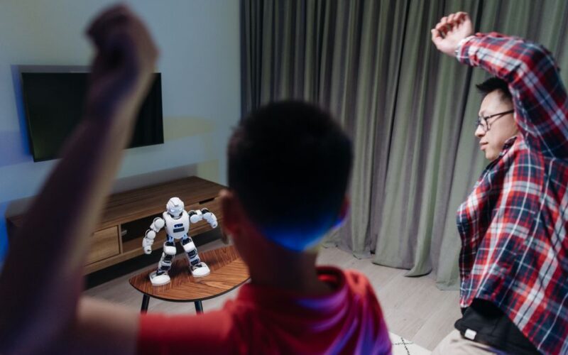 Father and son dancing enthusiastically with a toy robot at home, enjoying family time together.