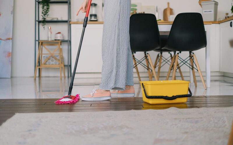 Side view of crop anonymous woman washing parquet with mop against bucket and carpet in house