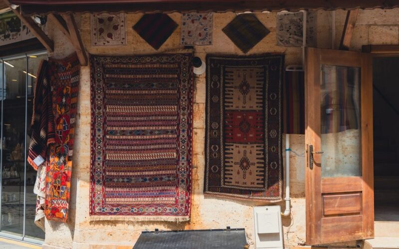 Handmade carpets hanging on an outdoor wall beside an open wooden door. A showcase of traditional craftsmanship.