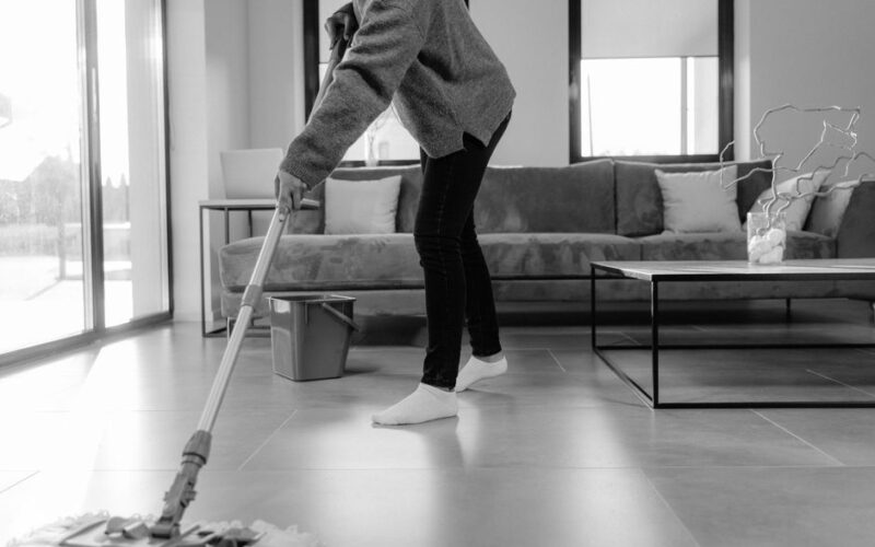 A grayscale photo of a person mopping the floor in a modern living room.