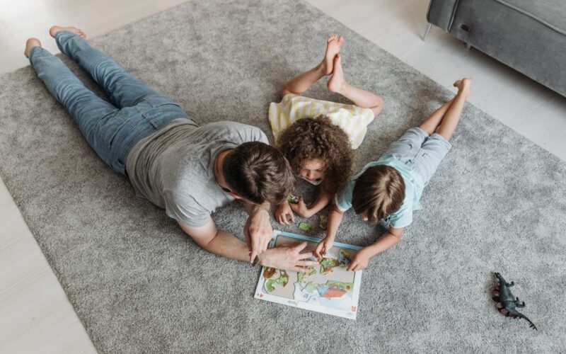 Father and kids enjoy quality time solving a puzzle together on a living room rug.