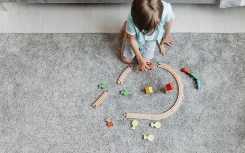 A child playing with a colorful toy train set on a living room carpet.