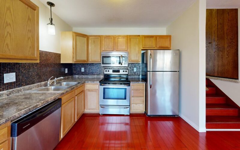 Contemporary kitchen interior featuring red floors, wooden cabinets, and stainless steel appliances.