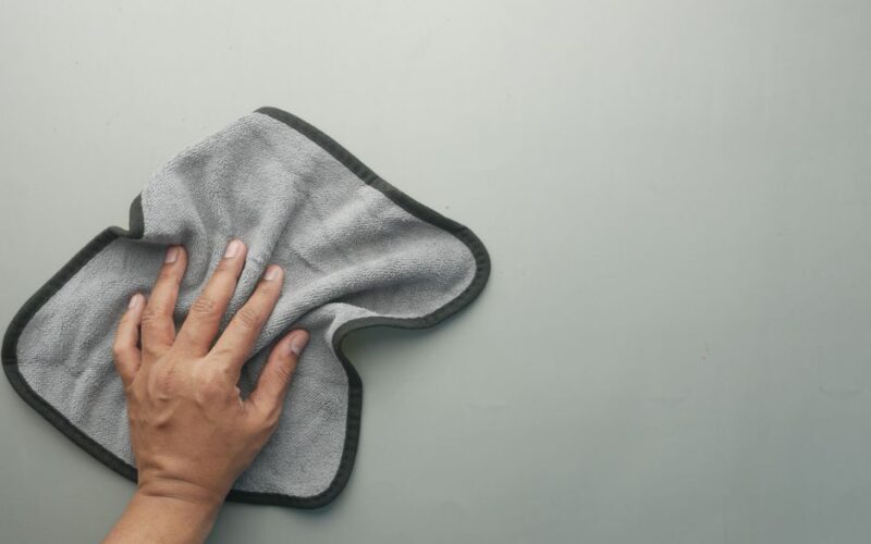 A hand wipes a light-colored table using a gray microfiber cloth, ideal for cleaning concepts.