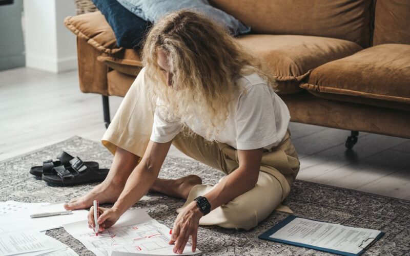 Woman sits on the carpet planning and drawing floor plans in a cozy living room.