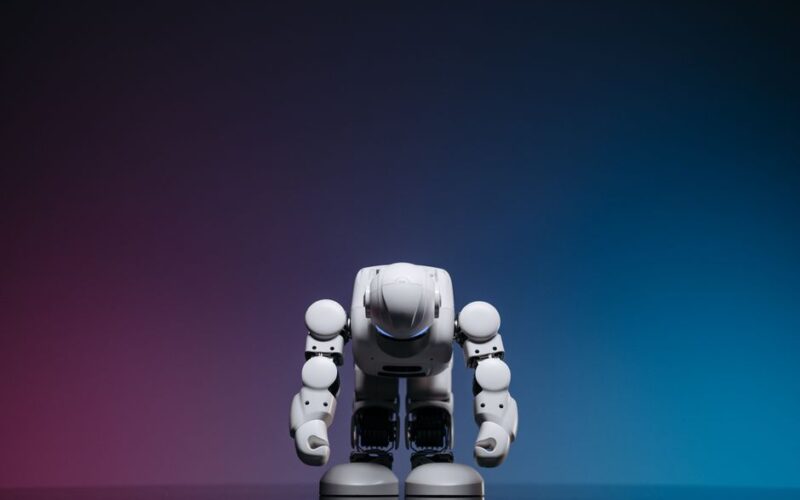 White robot in a bowing pose against a gradient studio background.