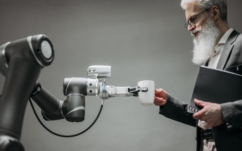 An elderly man receives a cup from a robotic arm in a modern office setting.