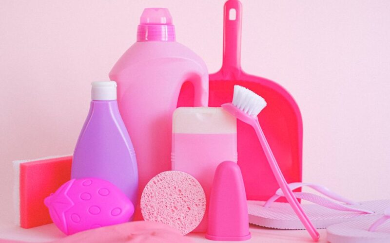 Assorted plastic containers with sponge and dustpan with brush for cleaning routine on pink background