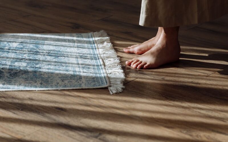 A pair of bare feet stands on a prayer rug in a sunlit room, capturing a serene and spiritual moment.