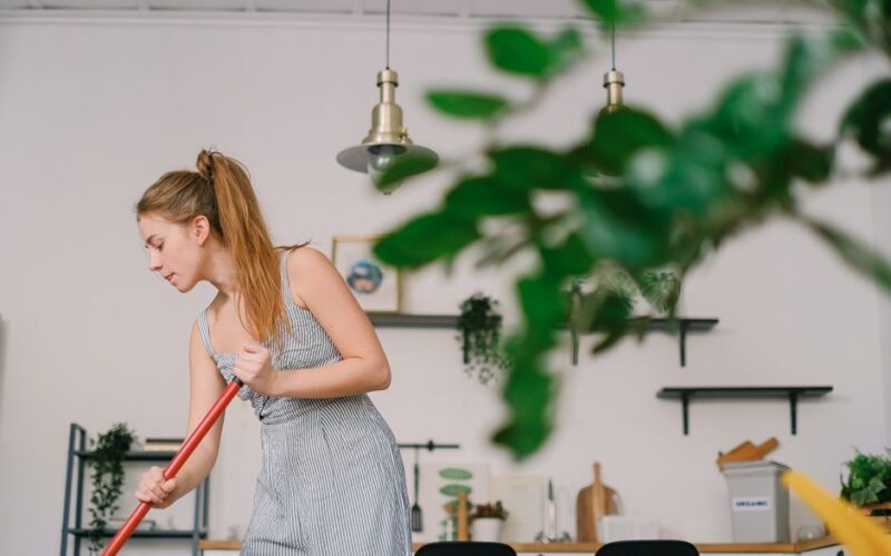 Young attentive female with brown hair cleaning floor while looking down in house kitchen in daytime