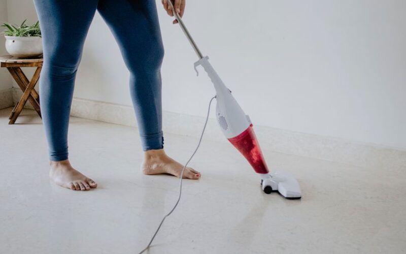 Close-up of a woman vacuuming a clean marble floor barefoot, showcasing home cleaning and maintenance.