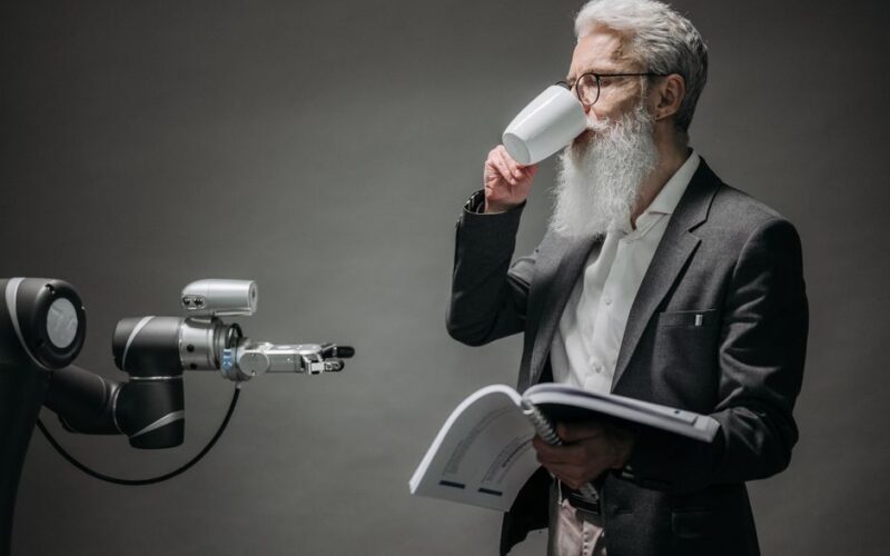 A senior man interacts with a robot while holding a book, symbolizing technology and innovation.