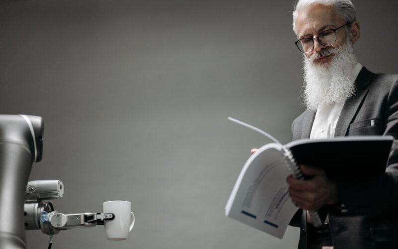Elderly man reads as a robotic arm holds a coffee cup, showcasing technology integration.
