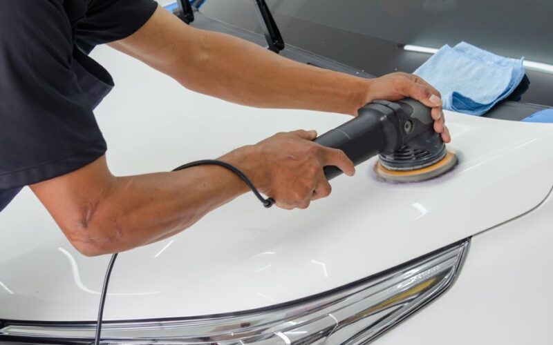 Close-up of a mechanic using a rotary polisher on a white car bonnet for detailing.