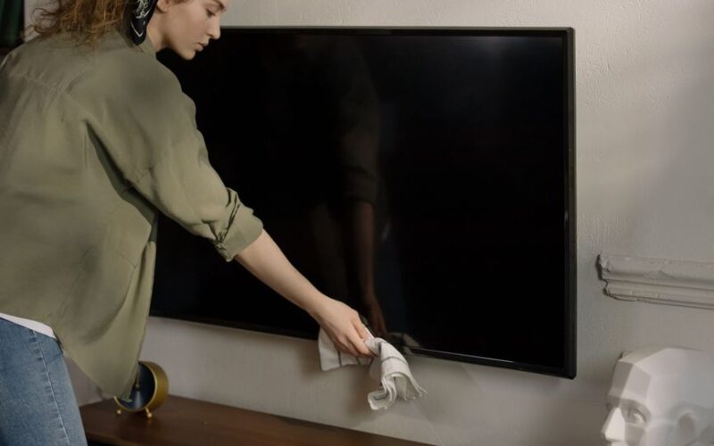 A woman cleaning a black screen TV in a cozy home environment, promoting cleanliness.