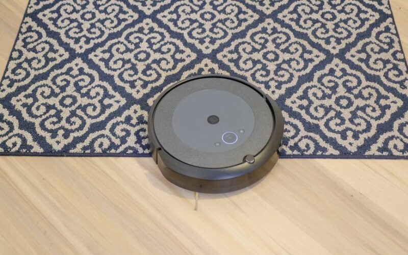 A modern robotic vacuum cleaning a stylish patterned carpet on a wooden floor.
