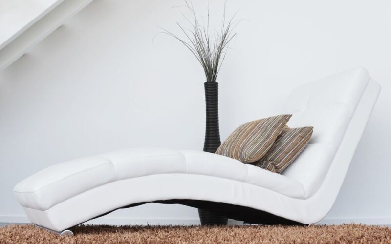 Elegant white lounge chair with cushions on plush carpet, perfect for relaxation.