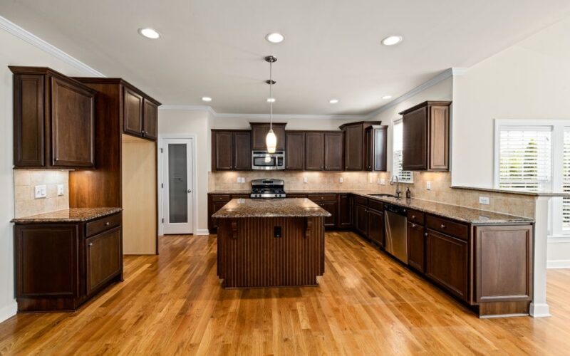 Luxurious wooden kitchen featuring dark cabinets, island, and stainless steel appliances.